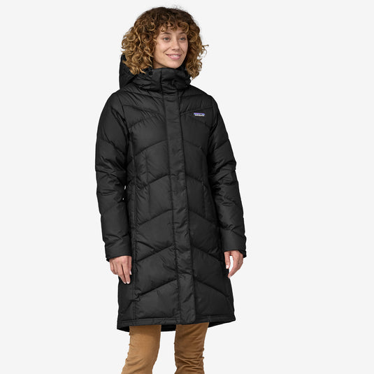 A woman wearing a knee-length black Patagonia parka with a removable hood and a two-way zipper.