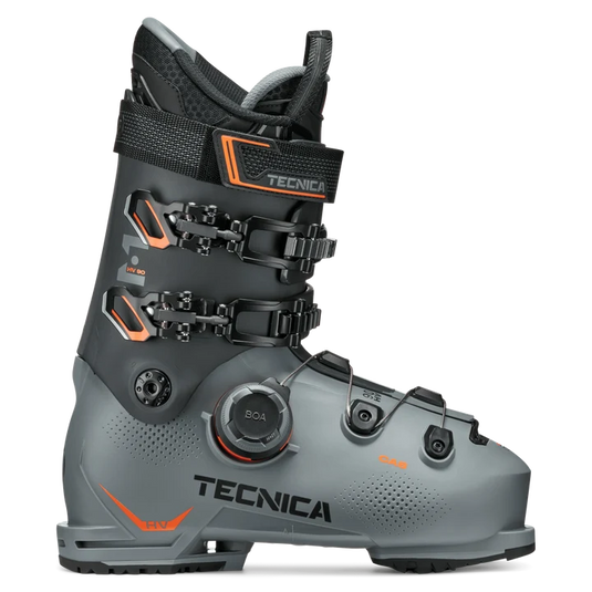 A single Tecnica ski boot in dark gray and black with bright orange accents, featuring dual quick-release buckles and a BOA dial system, shown on a clean white background. Ski and Tennis Station