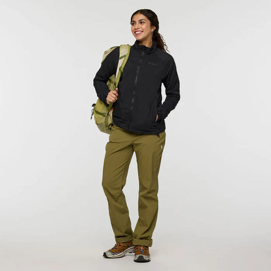 Woman wearing a black jacket and green pants holding a green backpack on a white background