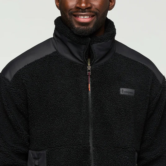 Man wearing a black fleece jacket with a cotopaxi logo on a light gray background