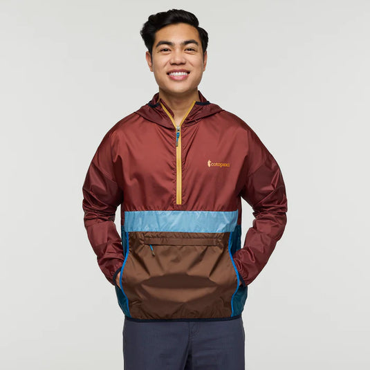 Man wearing a multicolored jacket with a cotopaxi logo on a plain background