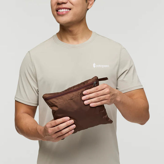 Person holding a brown zippered pouch with a jacket inside it on a plain background