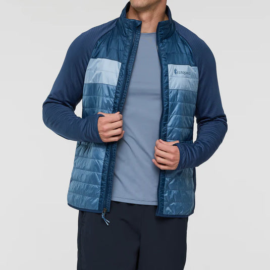 Person wearing a blue puffer jacket with a Cotopaxi logo on a light gray background