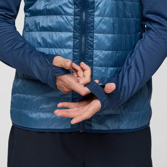 Person wearing a blue puffer jacket with thumb cuffs on a light gray background