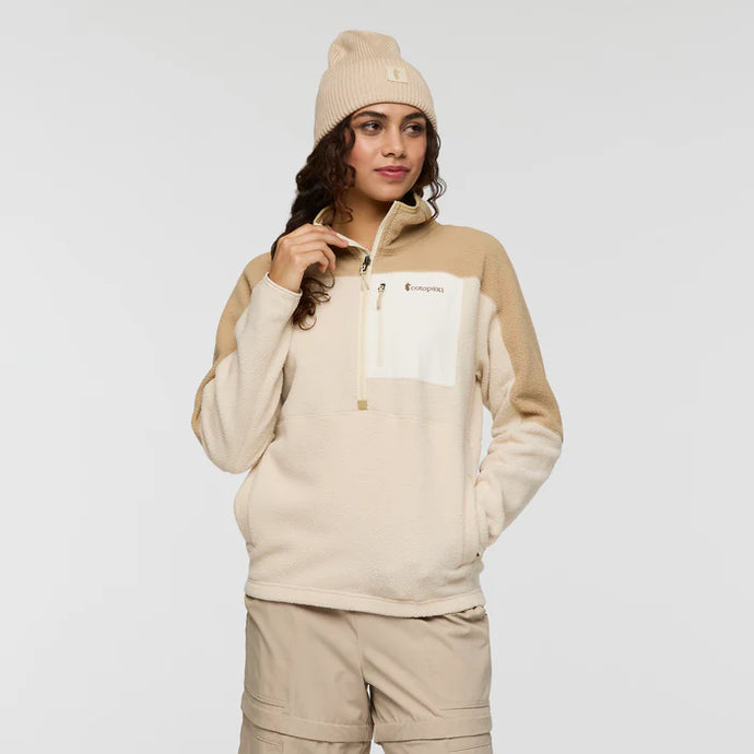 Woman wearing a beige and white fleece pullover with a logo on a light gray background