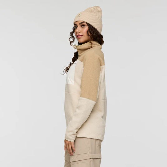 Woman wearing a beige and white color-blocked outfit with a matching beanie on a plain background