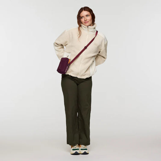 Woman wearing a cream jacket and dark pants with a purple bag on a white background