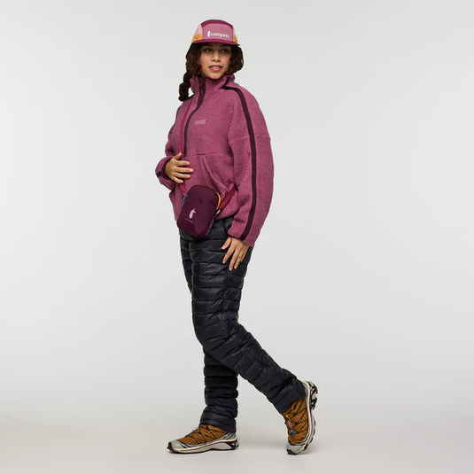 Person wearing a pink Cotopaxi jacket and black pants on a white background