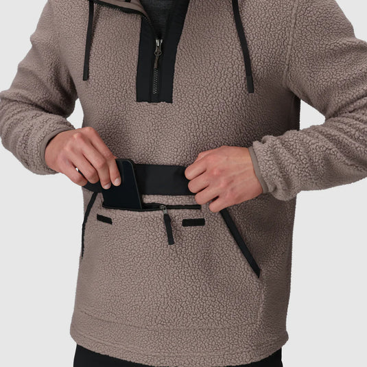 Person wearing a brown fleece pullover with a phone in a pocket on a light gray background