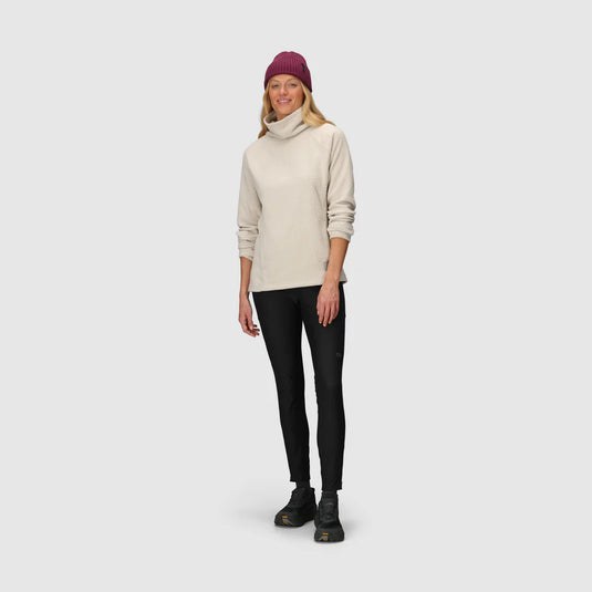 Woman wearing a beige turtleneck sweater, black leggings, and a purple beanie on a white background