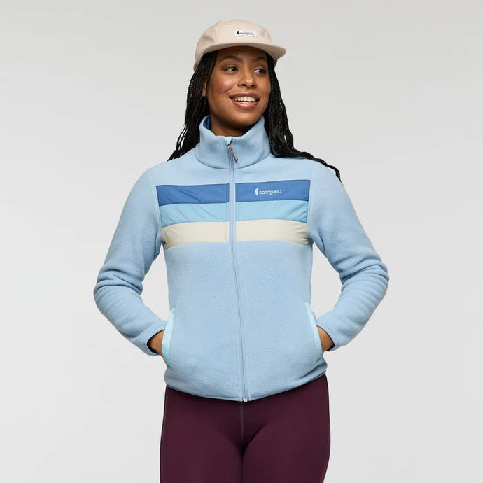 Woman wearing a light blue fleece jacket with a Cotopaxi logo on a plain background