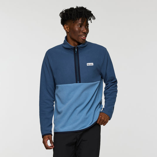 Man wearing a two-tone blue pullover with a visible brand logo on a light gray background