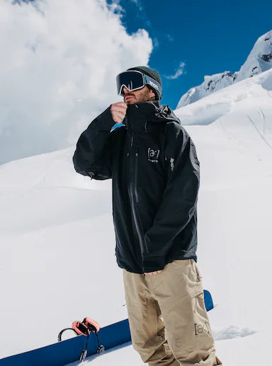 Load image into Gallery viewer, Person in Burton winter gear with a snowboard, standing on a snowy slope with mountains in the background.
