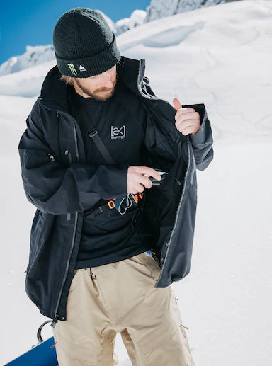 Load image into Gallery viewer, Man using interior protective pocker of Burton Gore-TEx Jacket with a snow-covered mountain background
