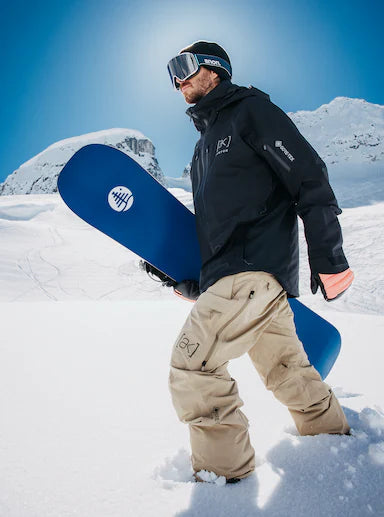 Person holding a blue snowboard in a snowy landscape with clear blue sky
