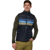 Man wearing a colorful puffer vest with a Cotopaxi logo on a white background