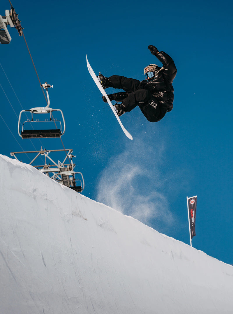 Load image into Gallery viewer, Person snowboarding off a jump with a chairlift in the background.
