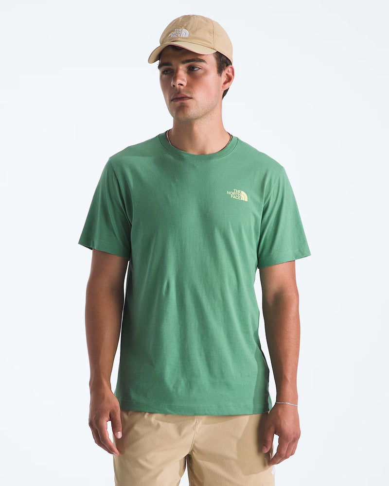 Load image into Gallery viewer, A man wearing a dimmed algae short-sleeve crewneck t-shirt by The North Face, paired with khaki pants and a beige baseball cap. Ski and Tennis Station
