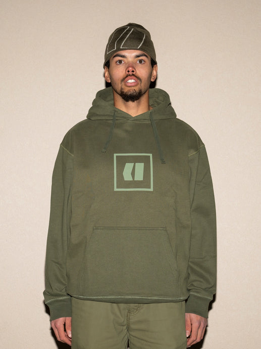 Person wearing a green hoodie with a logo on a beige background