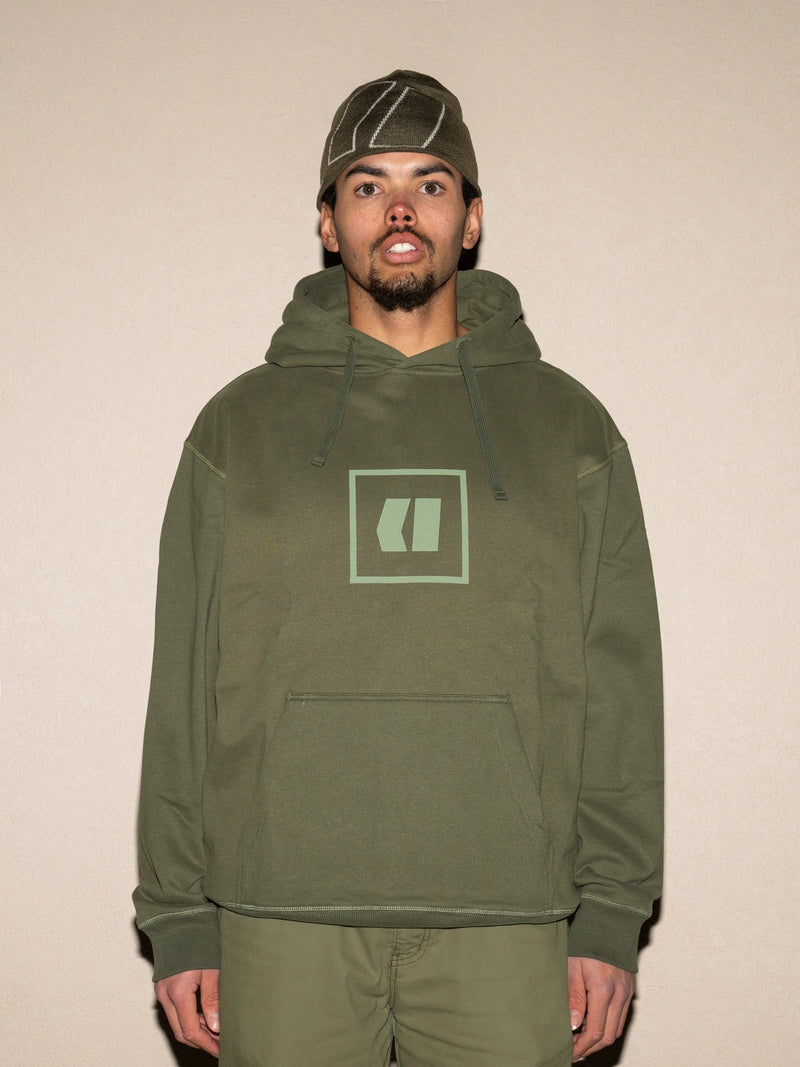 Load image into Gallery viewer, Person wearing a green hoodie with a logo on a beige background
