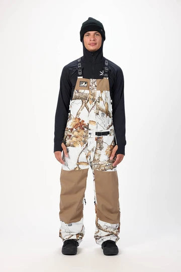 Load image into Gallery viewer, A model wearing Airblaster brown and white camouflage snow bib overalls with solid brown legs. Ski and Tennis Station
