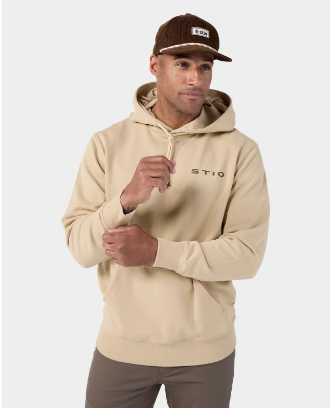 Load image into Gallery viewer, A man wearing a beige pullover hoodie with 'STIO' printed on the chest, paired with brown pants and a brown corduroy cap, against a light gray studio background. Ski and Tennis Station
