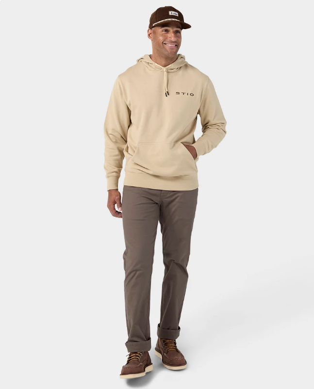 Load image into Gallery viewer, A man modeling a beige pullover hoodie with a small black STIO logo on the left chest, paired with brown pants and brown boat shoes. Ski and Tennis Station
