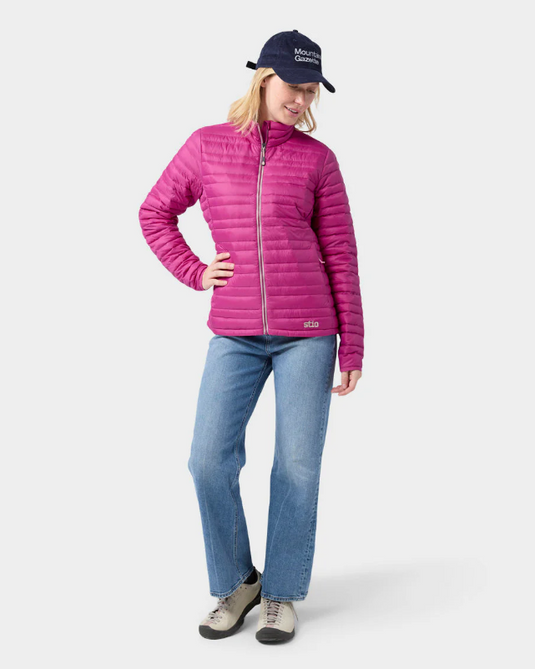 A woman wearing a bright pink Stio puffer jacket with a high collar and front zipper. Ski and Tennis Station