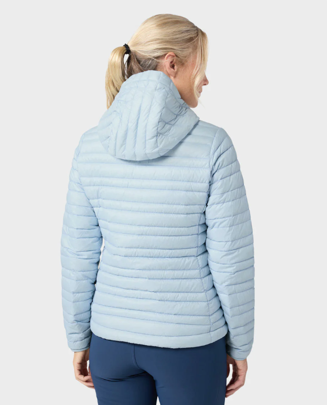 Load image into Gallery viewer, A woman modeling a light blue hooded Stio puffer jacket with a bright blue zipper, paired with navy blue leggings. Ski and Tennis Station
