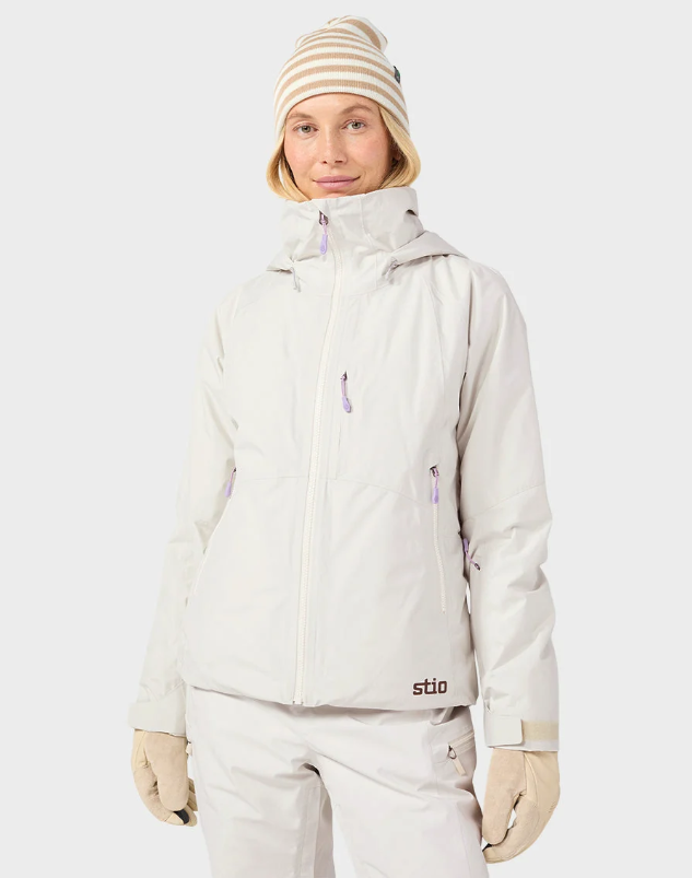 Load image into Gallery viewer, A model wearing a light beige/cream Stio ski jacket, matching ski pants. Ski and Tennis Station.
