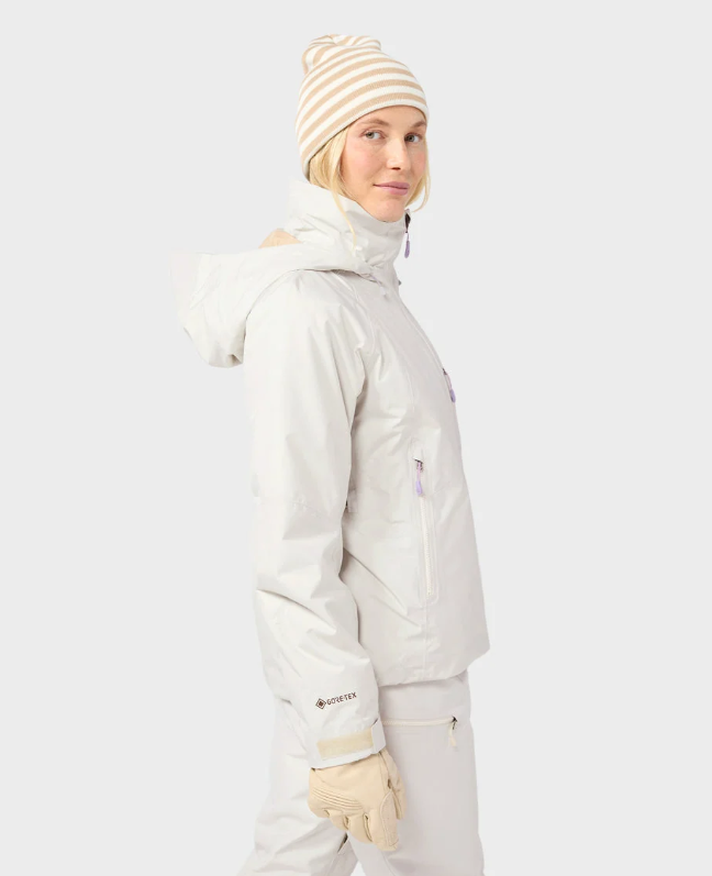 Load image into Gallery viewer, A model wearing a light beige/cream Stio ski jacket, matching ski pants. Ski and Tennis Station.
