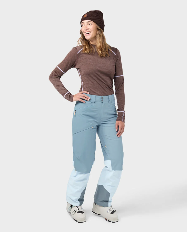Load image into Gallery viewer, A model wearing light blue and white color-blocked Stio skyrider ski pants with a brown long-sleeve top and white ski boots. Ski and Tennis Station
