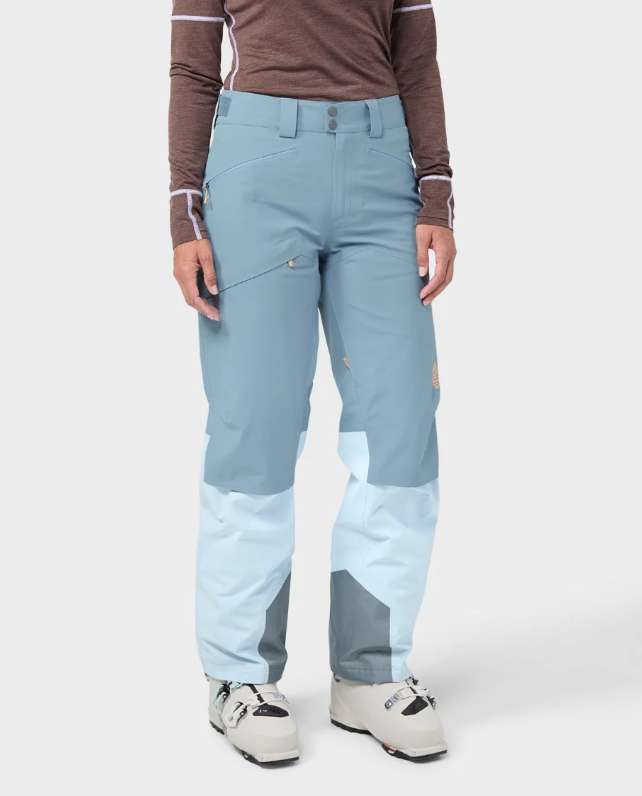 Load image into Gallery viewer, A model wearing light blue and white color-blocked Stio skyrider ski pants with a brown long-sleeve top and white ski boots. Ski and Tennis Station
