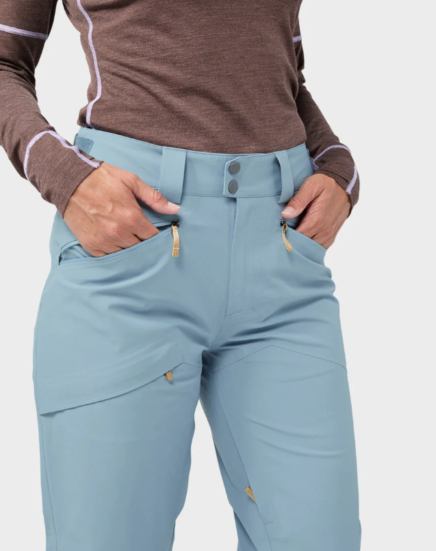 Load image into Gallery viewer, A model wearing light blue and white color-blocked Stio skyrider ski pants with a brown long-sleeve top and white ski boots. Ski and Tennis Station
