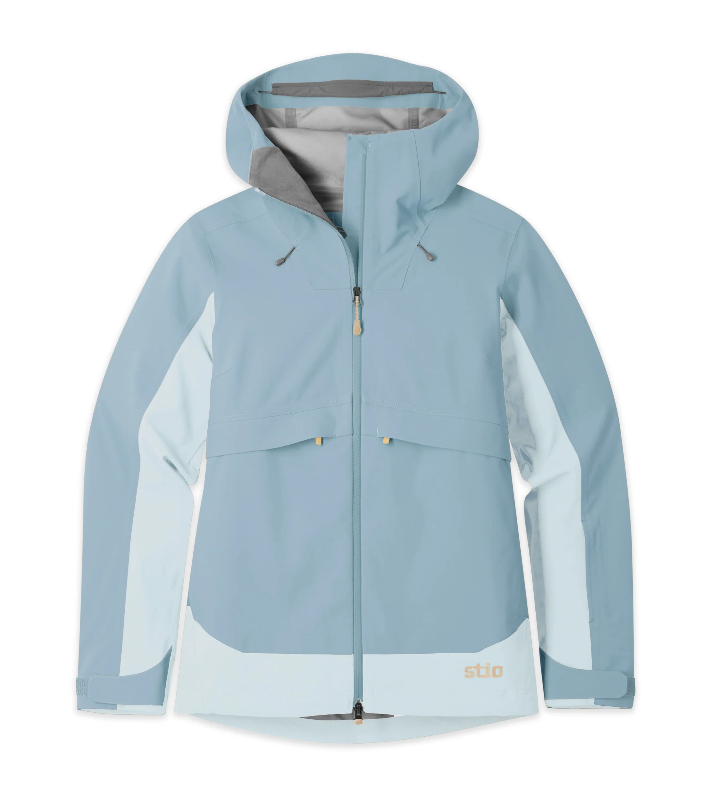 Load image into Gallery viewer, A light blue hooded technical jacket with contrasting pale blue and white panels on the sleeves and lower hem, featuring a full-length front zipper and a small orange 'stio' logo near the bottom right. Ski and Tennis Station
