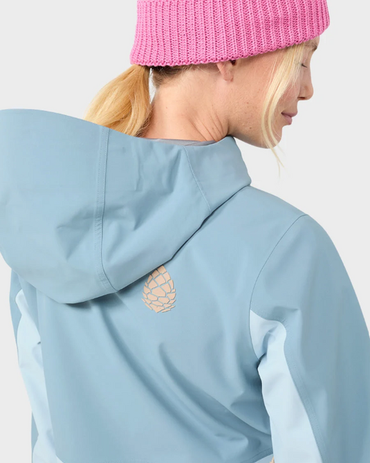 A close-up side profile of a model wearing a light blue hooded jacket and a pink knit beanie against a plain light gray background.