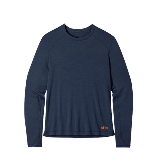 A navy blue long-sleeve performance shirt with raglan sleeves and a small orange 'stio' logo near the bottom right hem, Ski and Tennis Station