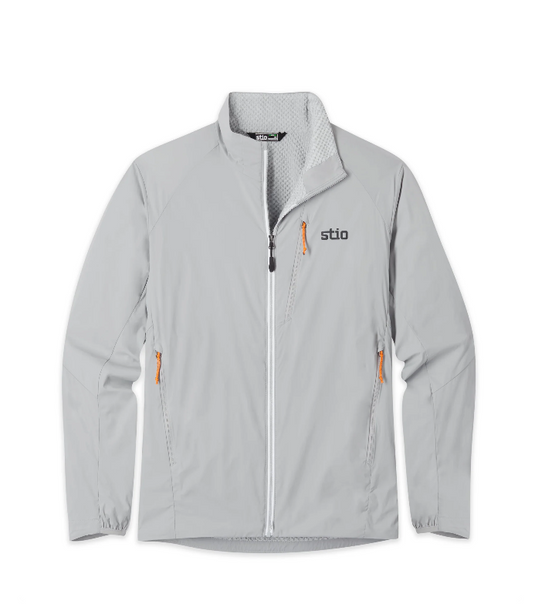 A light gray zip-up jacket with a high collar, featuring a black and gray 'stio' logo on the left chest and bright orange zipper pulls, shown against a plain white background. Ski and Tennis Station