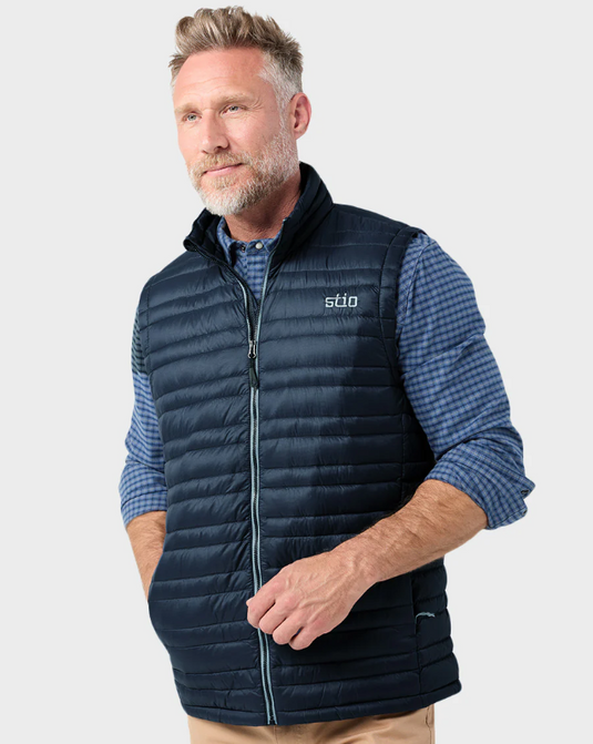 A man wearing a navy blue quilted Stio zip-up vest over a blue and white checkered long-sleeve shirt. Ski and Tennis Station