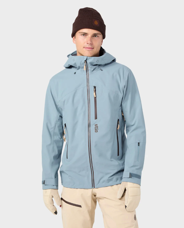 Load image into Gallery viewer, A man wearing a light blue hooded Stio ski jacket, beige ski pants, a dark brown beanie, and beige gloves. Ski and Tennis Station.
