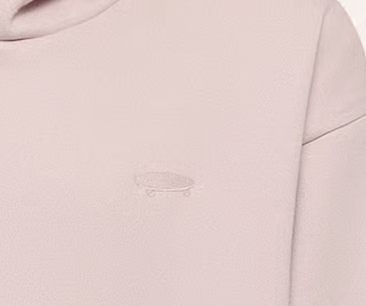 Close-up of a light blush pink sweatshirt featuring a small, tonal embroidered skateboard logo on the chest.