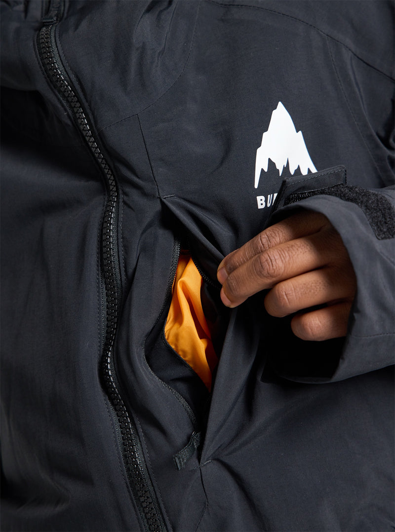 Load image into Gallery viewer, Close-up of a person opening a black Burton jacket pocket with a visible brand logo.
