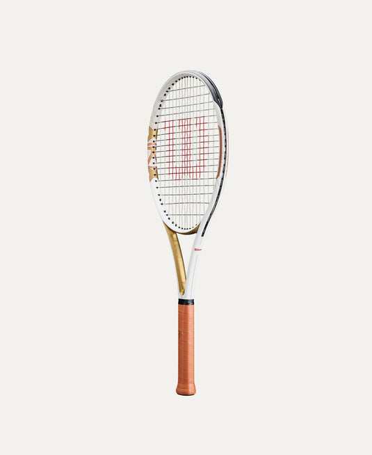 A Wilson Roger Federer HOF tennis racket with a white and gold frame, red string pattern, and a brown grip, shown vertically against a light beige background. Ski and Tennis Station.