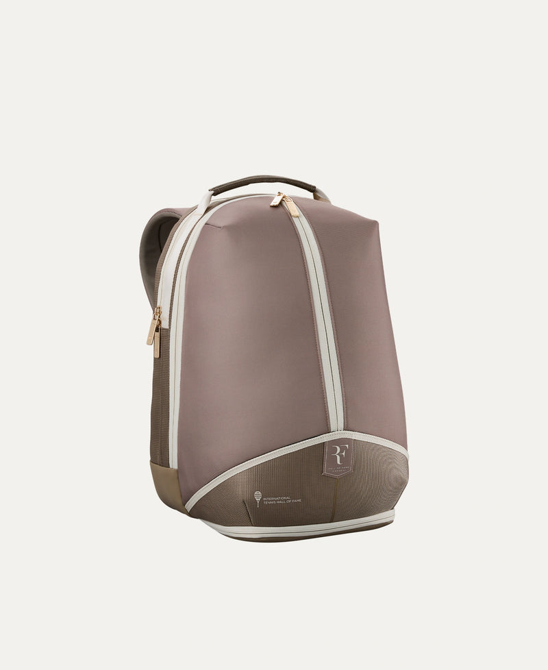 Load image into Gallery viewer, A minimalist Roger Federer Hall of Fame backpack in a muted taupe-brown color with cream-colored piping and gold-tone zipper pulls, shown from a three-quarter angle against a solid off-white background. Special Edition. Ski and Tennis Station.
