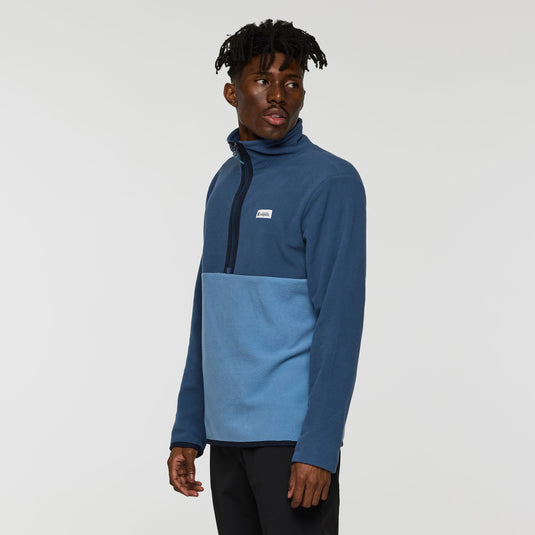 Person wearing a blue and gray pullover with a visible brand logo on a white background