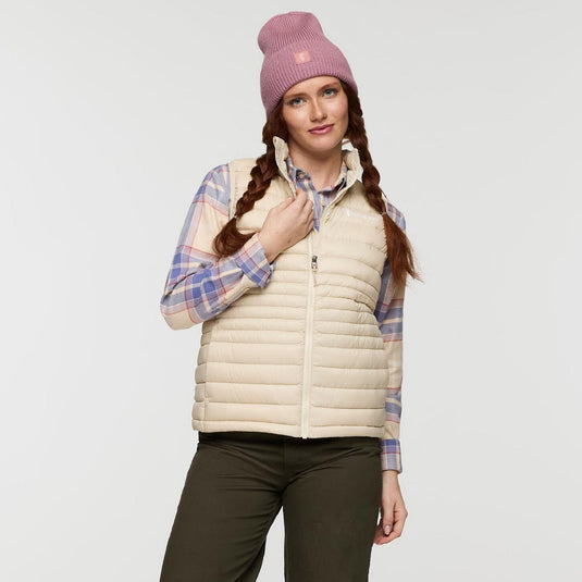 Woman wearing a beige puffer vest, plaid shirt, and pink beanie on a white background